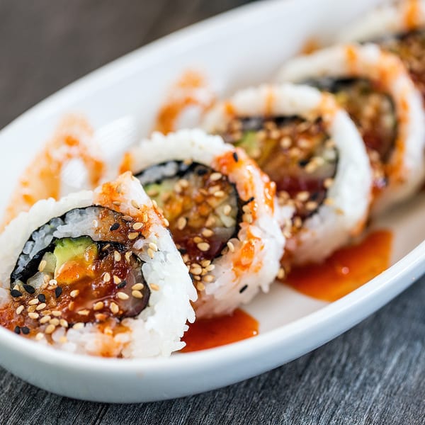 Sushi rolls with sesame seeds and orange sauce on a white platter.