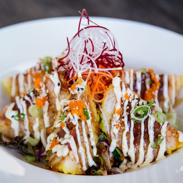 Triangular sushi pieces topped with white sauce, orange roe, and shredded vegetables on a white plate.