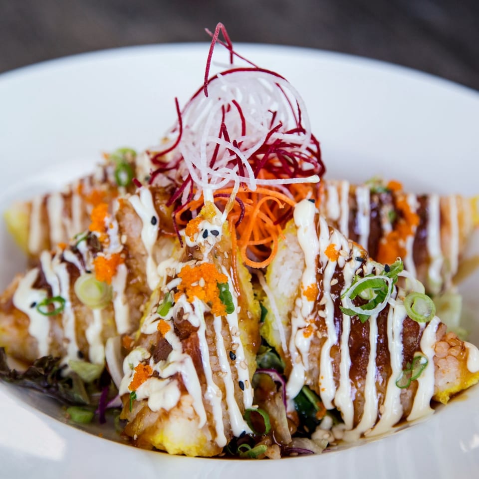 Triangular sushi pieces topped with white sauce, orange roe, and shredded vegetables on a white plate.