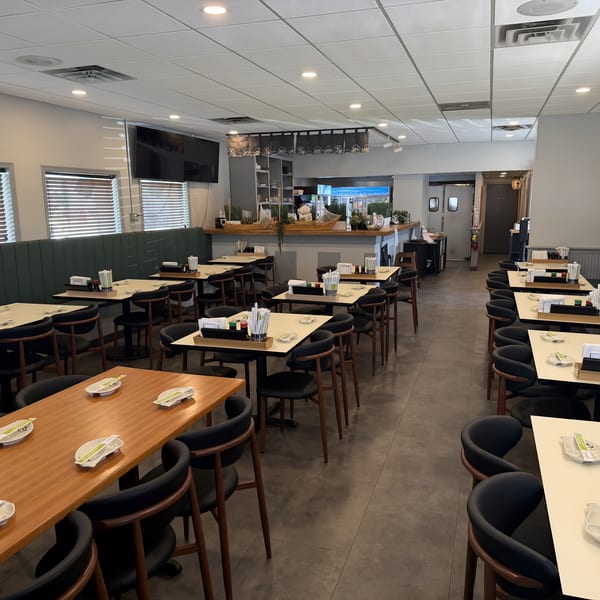 A brightly lit, empty restaurant dining room with tables, chairs, and booth seating.