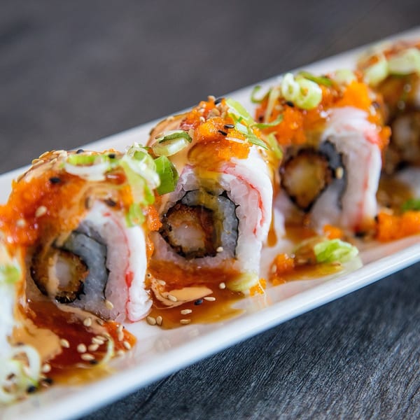 Sushi rolls with shrimp tempura, crab, roe, scallions, and sauce on a white plate.
