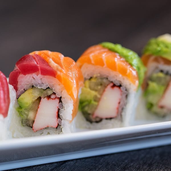 Close-up of colorful sushi rolls with tuna, salmon, avocado, and crab on a white plate.