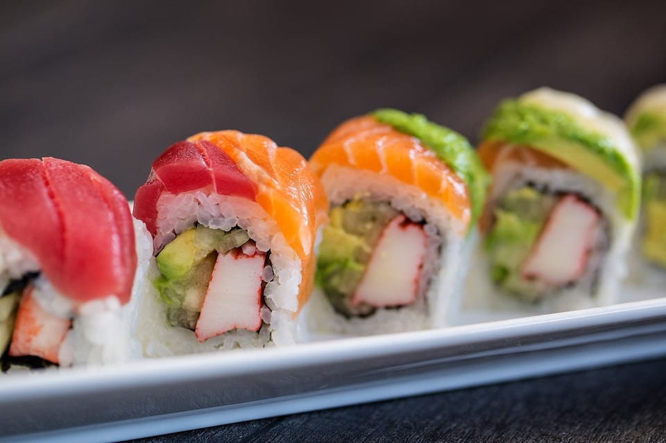 Close-up of colorful sushi rolls with tuna, salmon, avocado, and crab on a white plate.