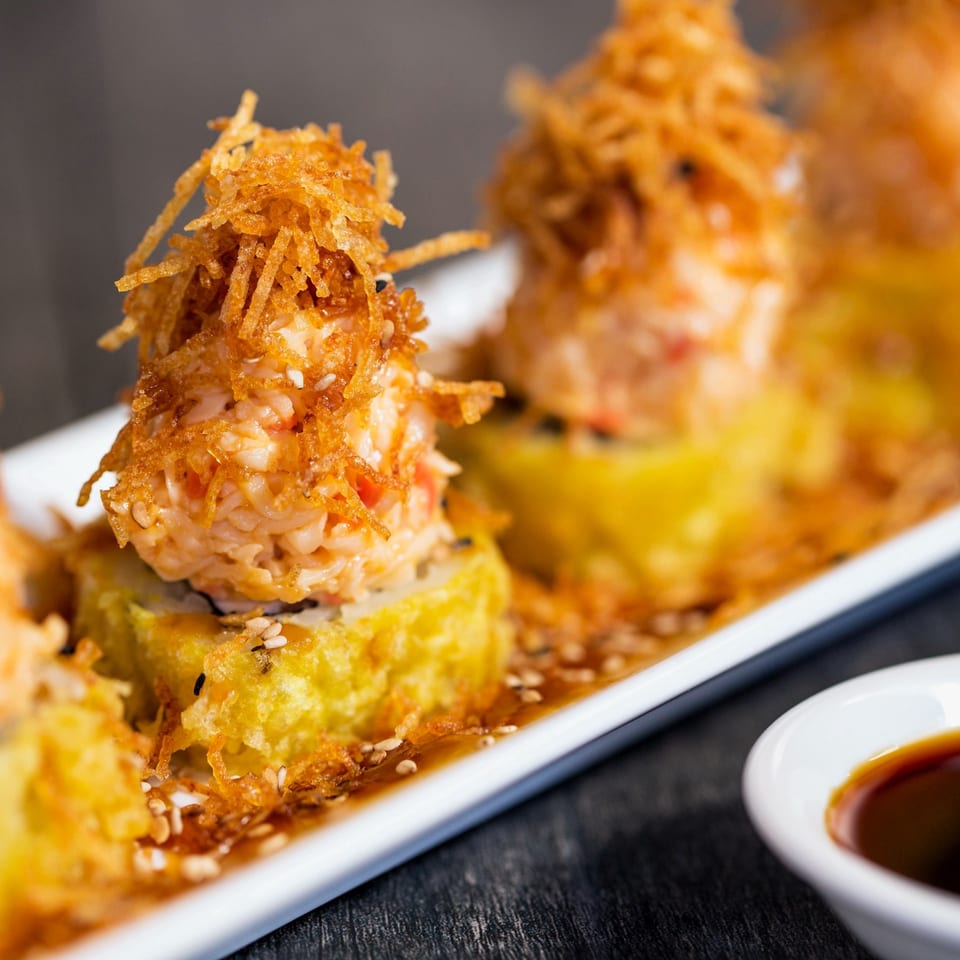 Four crispy, golden-fried sushi rolls topped with spicy crab and crunchy fried potato strings.