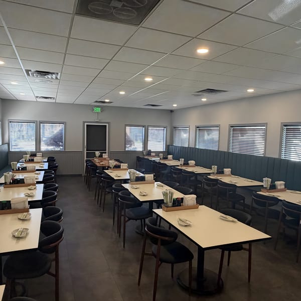 Empty restaurant dining room with rows of tables, chairs, and booths, set with chopsticks and dishes.