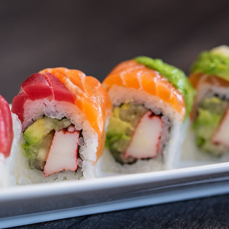 Colorful sushi rolls with tuna, salmon, avocado, and crab meat on a white rectangular plate.