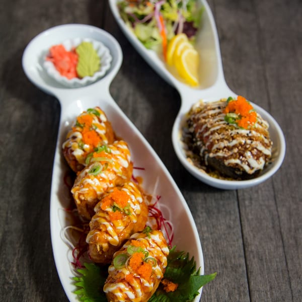 Three white dishes of Japanese appetizers, including fried rolls, salad, and a rice dish, on a wooden table.